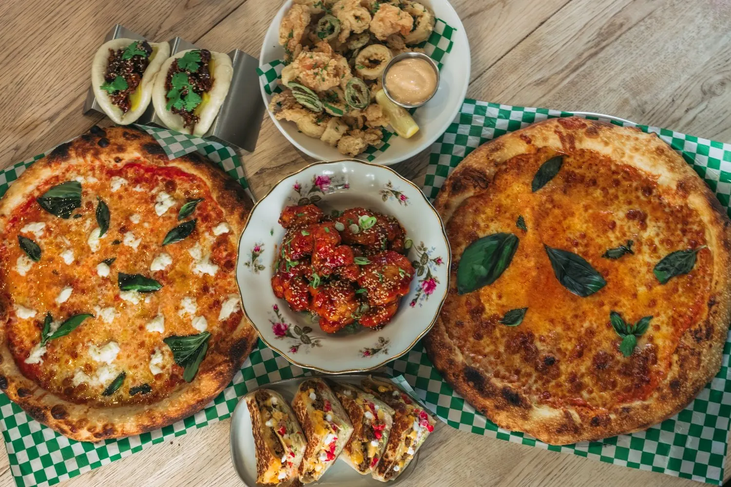 Pizzas and small plates on a green checkered tablecloth